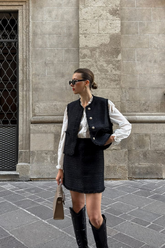 a lady in a ruffle collared shirt, a black tweed vest and a black tweed skirt